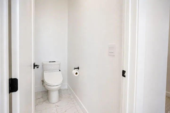 Modern half bath featuring a contemporary toilet with integrated bidet functionality, neutral tile flooring, and clean white walls with recessed lighting and electrical outlet access