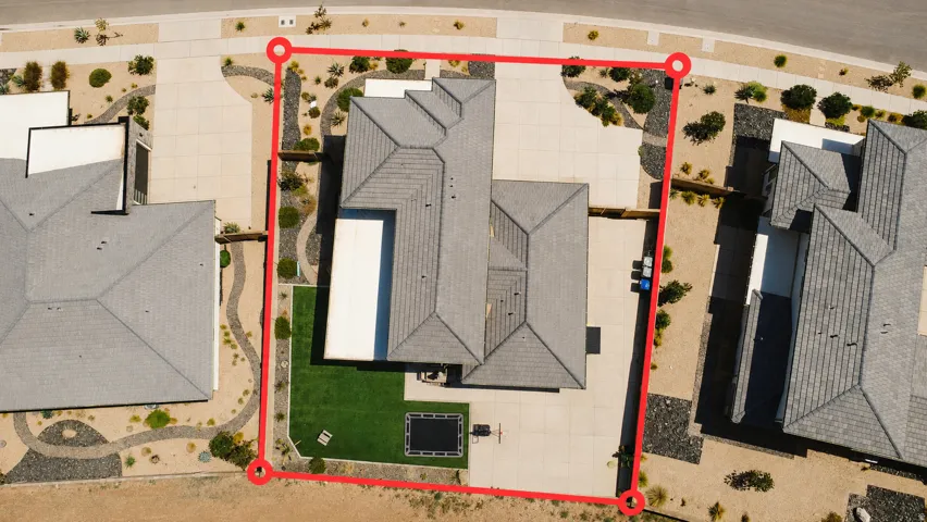 Aerial view showcasing a modern residence with a clean geometric roofline, expansive manicured lawn, mature landscaping throughout the property perimeter, and defined hardscaped borders framing the home's footprint