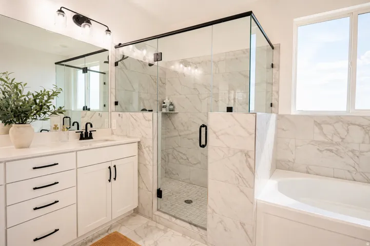 Spa-inspired primary bathroom showcasing marble-finish wall and floor surfaces, a frameless glass-enclosed walk-in shower with integrated bench seating, a freestanding soaking tub, and a dual-sink vanity with soft-close cabinetry and matte black hardware