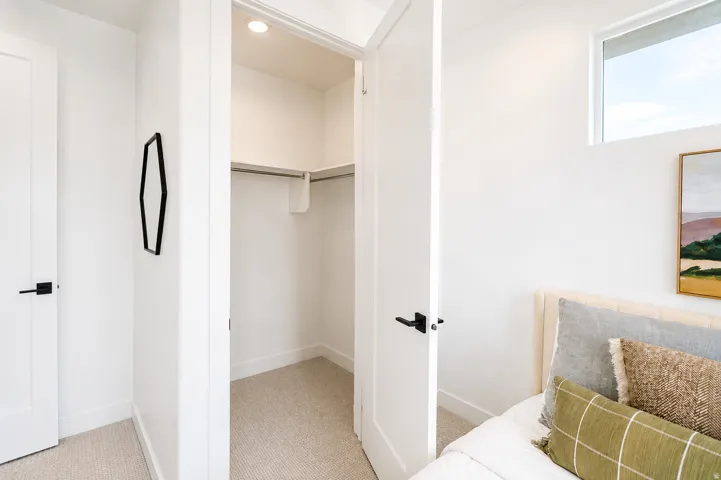 White interior door with black hardware, recessed ceiling light in closet, horizontal window, white walls, light-colored carpeting