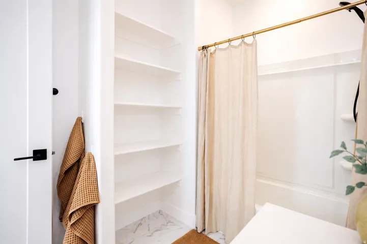 Built-in shelving for storage, white acrylic shower surround, and gold-finish shower rod