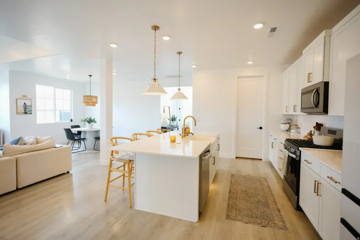Open-concept kitchen featuring an island with bar seating, white cabinetry, integrated stainless steel appliances, and wood-finish flooring