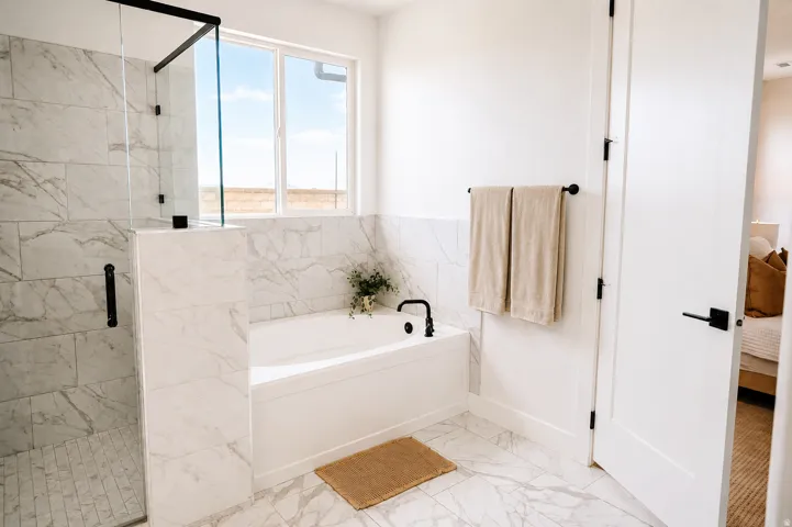 Walk-in shower with clear glass enclosure, a built-in soaking tub with matte black fixtures, white rectangular floor tiles, and a large window