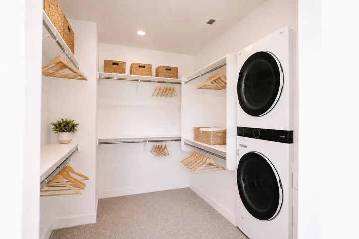 Walk-in closet with integrated shelving, ample hanging rods, and a stacked washer and dryer unit