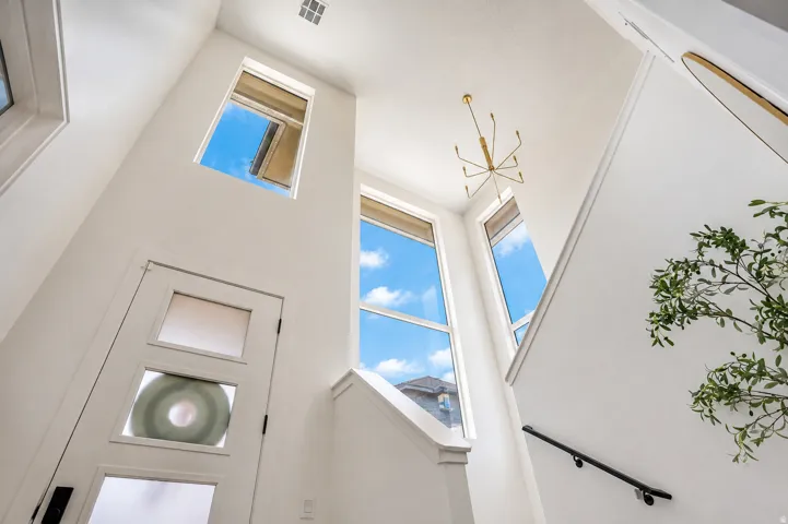 Vaulted ceiling with a contemporary chandelier, multiple transom windows, and a white paneled entry door with frosted glass inserts