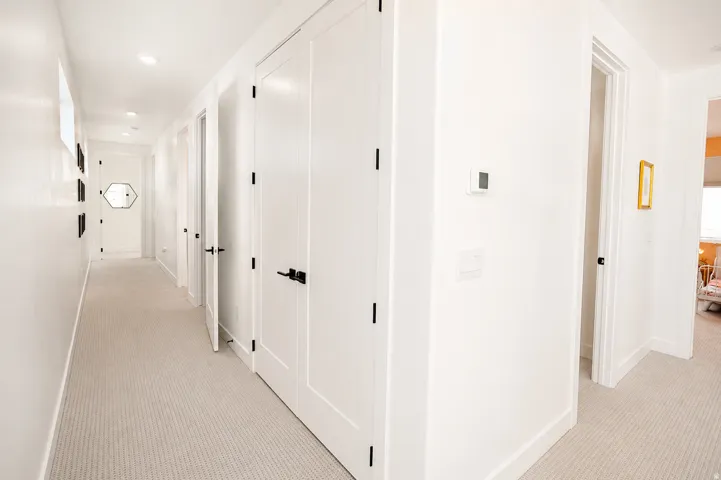 Hallway featuring light-colored carpeting, white interior doors with matte black hardware, and recessed lighting