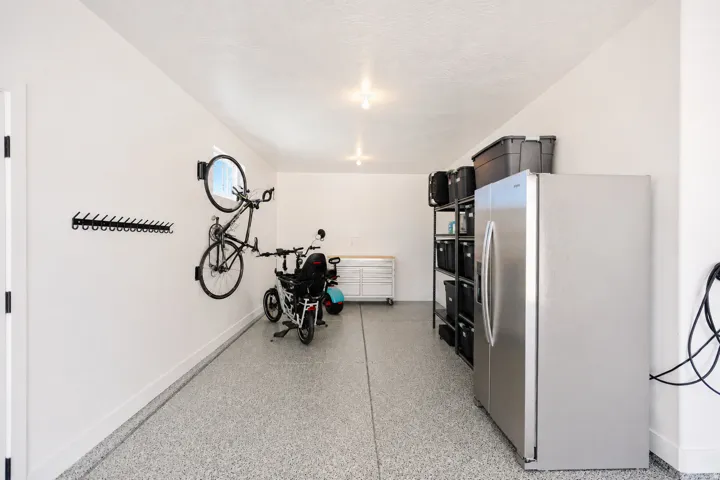 Spacious garage featuring epoxy-coated flooring, stainless steel refrigerator, wall-mounted bike storage, and recessed ceiling lighting
