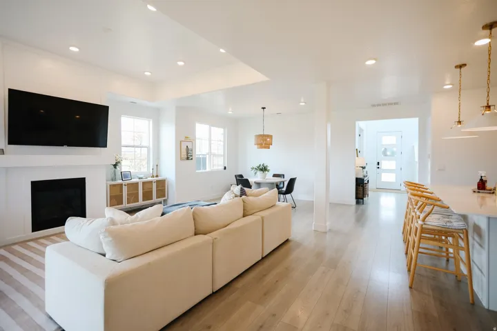 Integrated living space featuring wood-finish flooring, a contemporary fireplace with a white mantel, recessed lighting, and multiple windows