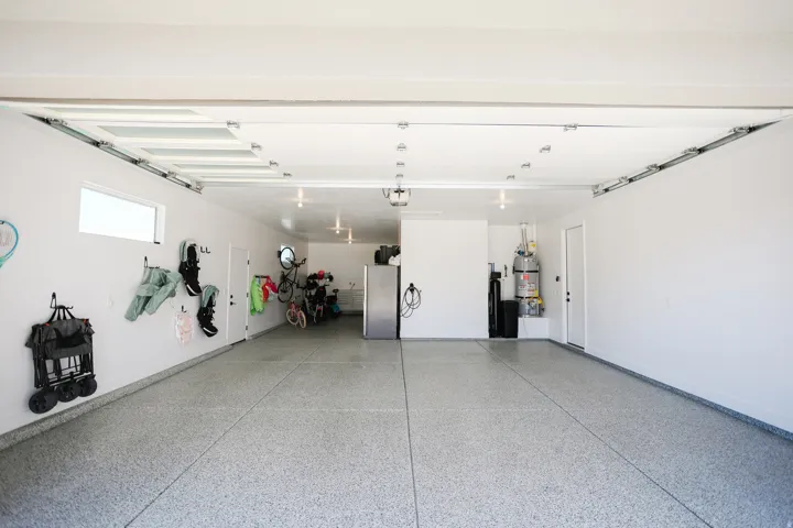 Expansive garage featuring a light gray speckled epoxy floor, white walls, flush-mounted lighting, and a horizontal window