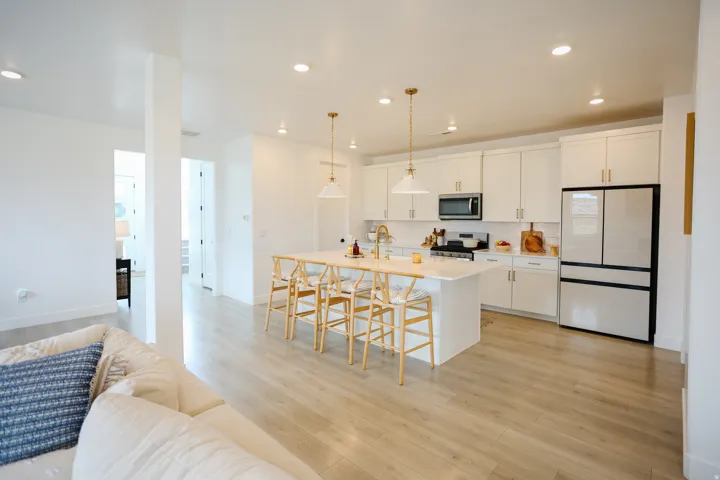 Open-concept kitchen and living area featuring white cabinetry, stainless steel appliances including a French-door refrigerator, quartz countertops, a large center island with seating for multiple, wood-finish flooring throughout, and recessed ceiling lig