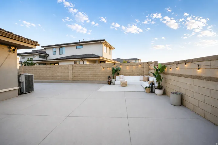 Expansive concrete patio with block privacy fencing, accented by string lighting, and mature potted plants