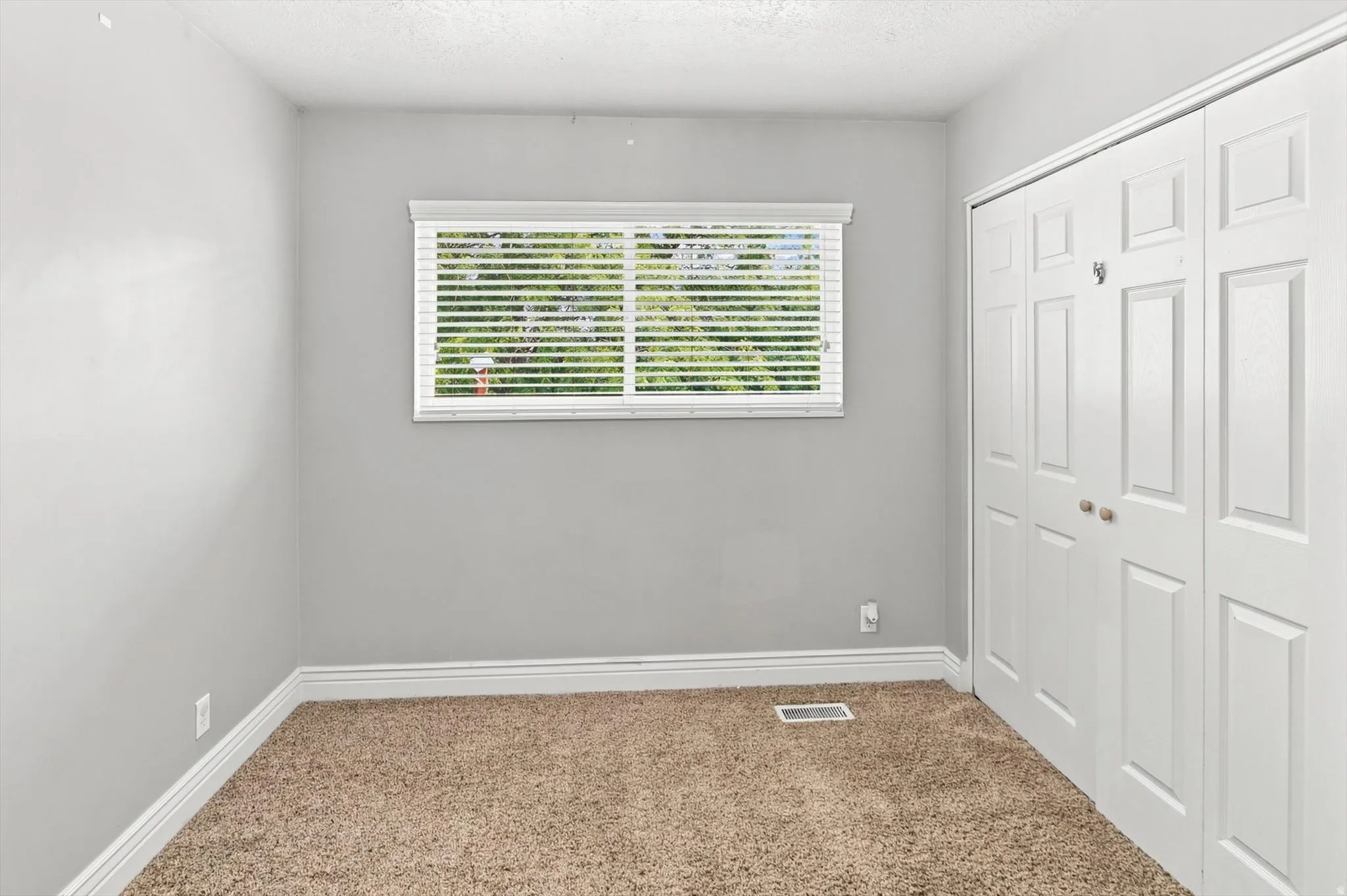 Neutral gray wall color, textured carpet flooring, and white bi-fold closet doors