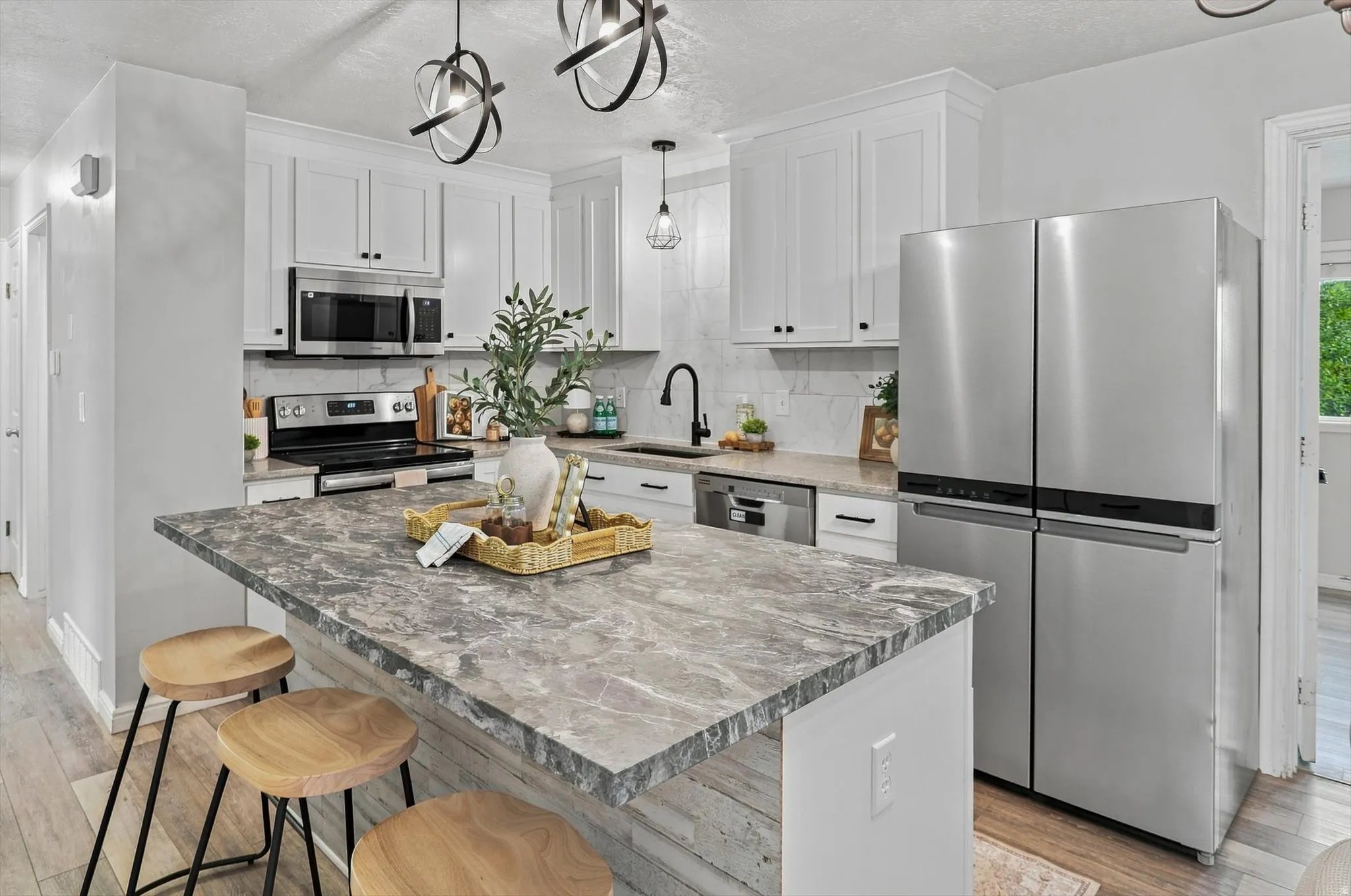 Kitchen featuring an island with a stone-finish countertop, white cabinetry with black hardware, stainless steel appliances, and wood-finish flooring