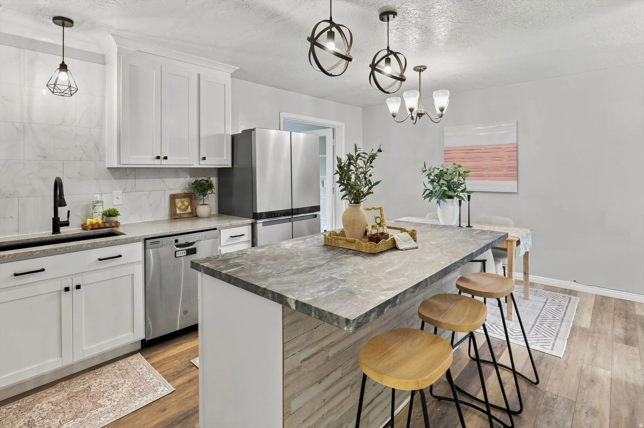 Spacious kitchen featuring an extended island with a stone-finish look countertop, crisp white cabinetry, stainless steel appliances, and wood-finish flooring