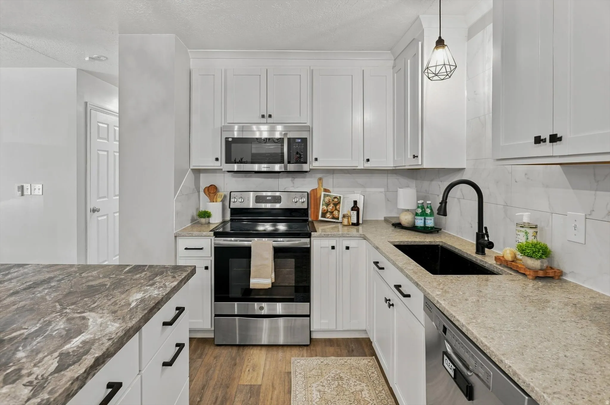Modern kitchen featuring white shaker cabinetry, stainless steel appliances, a tile backsplash, light-colored countertops, and a black sink with a matte black faucet