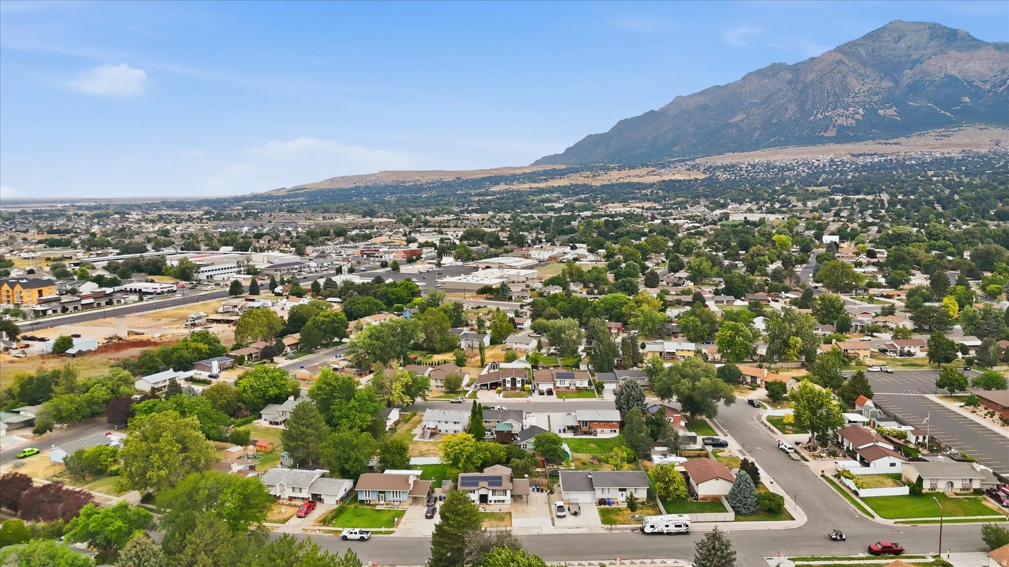 Aerial perspective of a residential community featuring numerous homes, mature trees, and a prominent mountain range backdrop