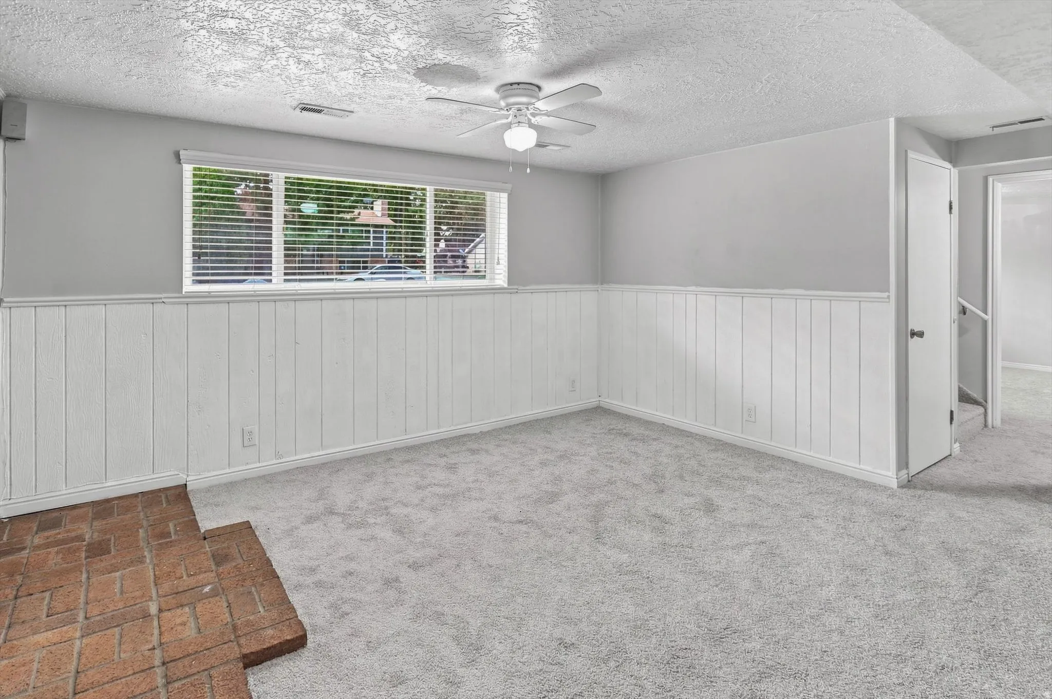 Spacious room featuring light gray carpet, white wainscoting, and a multi-pane window