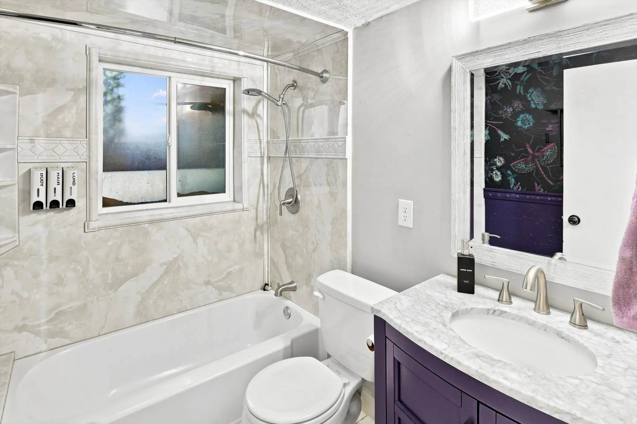 Bathroom featuring a white bathtub, a window with natural light, and a vanity with a white marble countertop