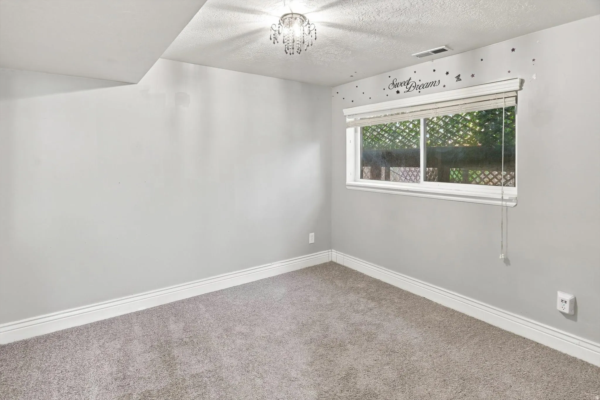 Carpeted room featuring a window with blinds, white baseboards, and a crystal chandelier