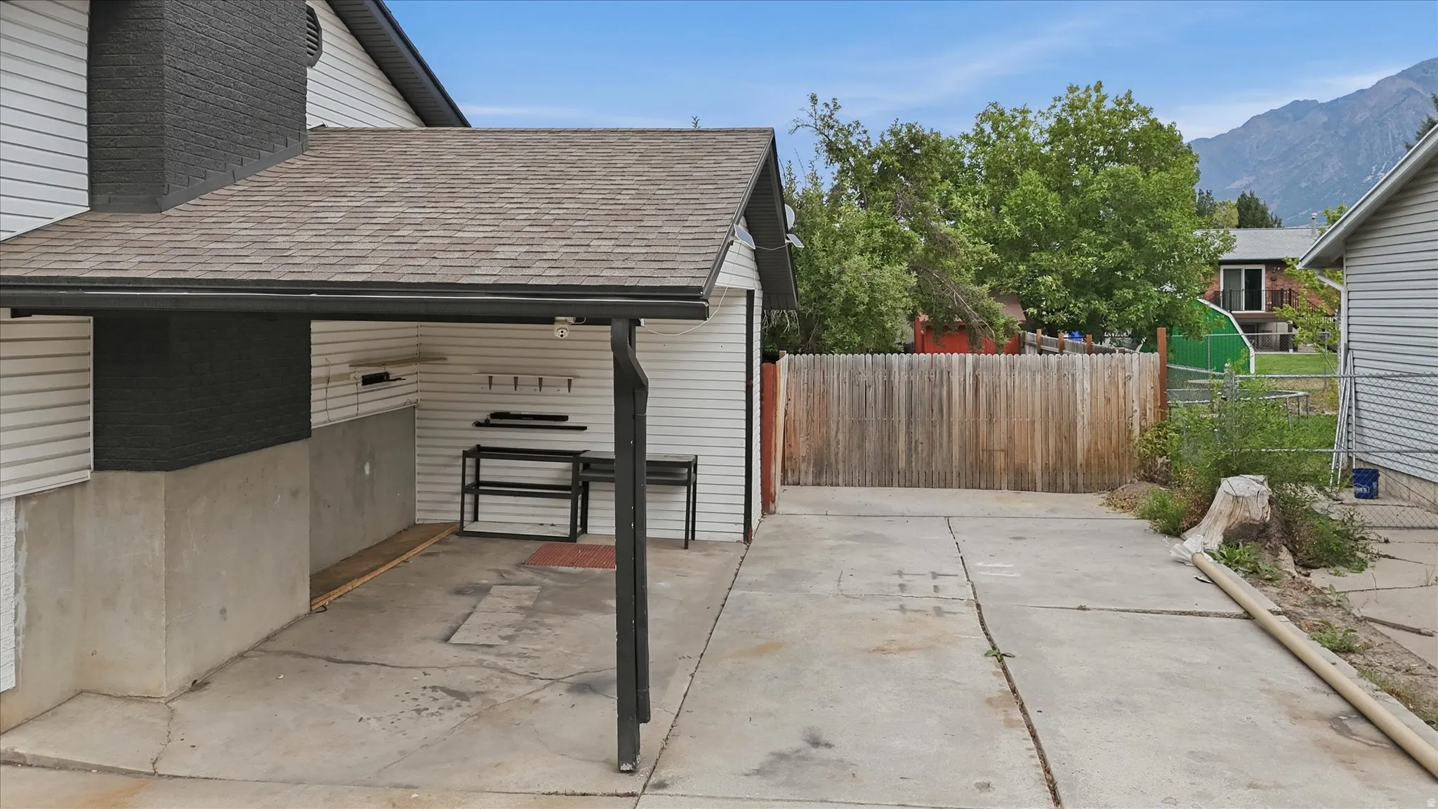 Covered outdoor area with concrete slab, white siding, and a partial wood fence