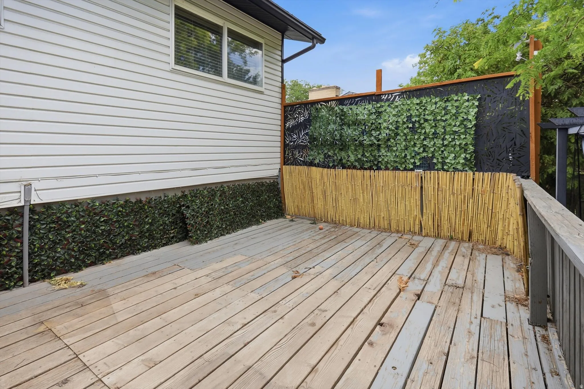 Expansive outdoor deck featuring wood-finish flooring, a decorative bamboo screen, and a privacy wall with intricate laser-cut patterns and faux greenery accents