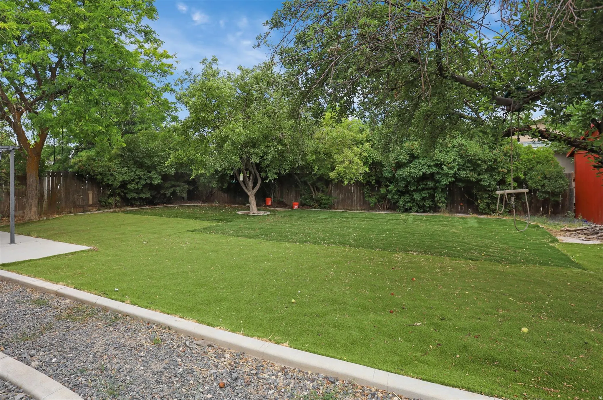 Expansive artificial green lawn with mature trees and a privacy fence