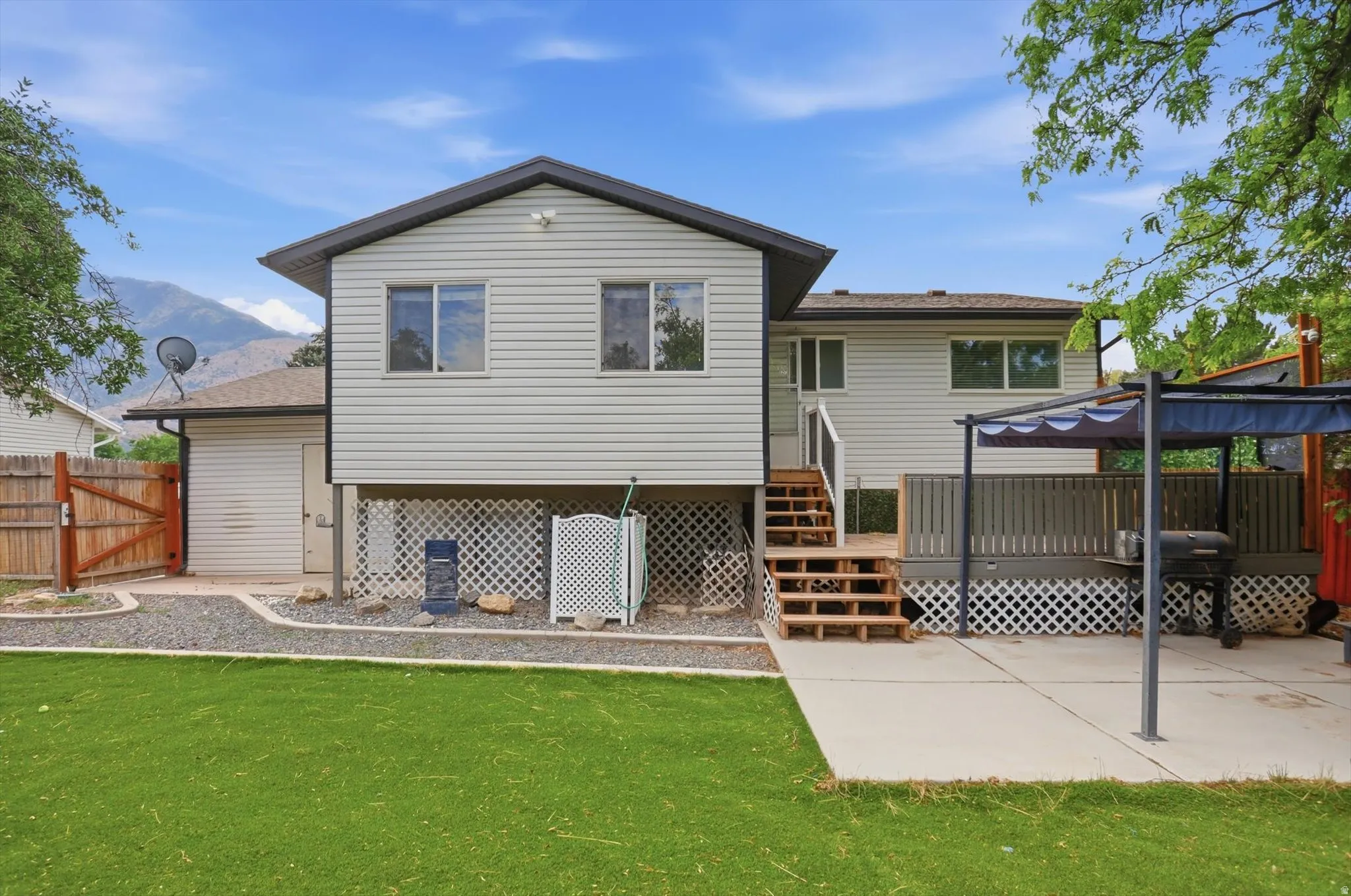 Rear exterior featuring a spacious artificial lawn, extended concrete patio, and private wood deck