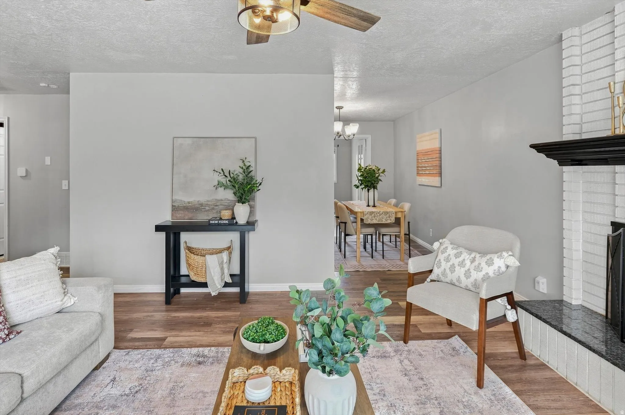 Living area featuring wood-finish flooring, a fireplace with a white brick surround and black mantel, and a ceiling fan with integrated lighting