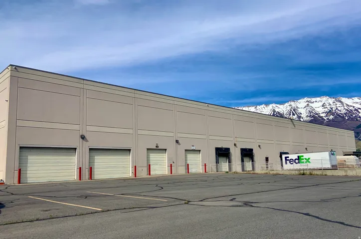 Expansive industrial building featuring multiple roll-up doors, a large paved parking area, and loading docks