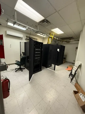 Commercial space featuring multiple server racks, suspended cable trays, and drop ceiling with integrated fluorescent lighting