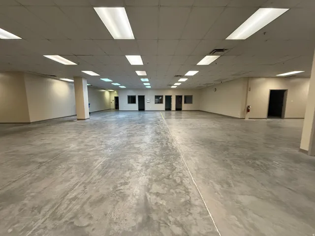 Expansive open-concept commercial space featuring concrete flooring, neutral-toned walls, and abundant overhead fluorescent lighting