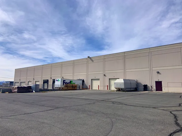 Expansive commercial building featuring multiple dock-high loading doors, multiple ground-level roll-up doors, an asphalt paved parking area, and an additional personnel entry door