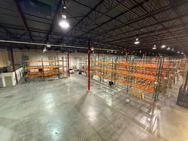 Spacious industrial warehouse featuring polished concrete flooring, extensive pallet racking systems, high ceilings with exposed structural beams, and integrated overhead lighting