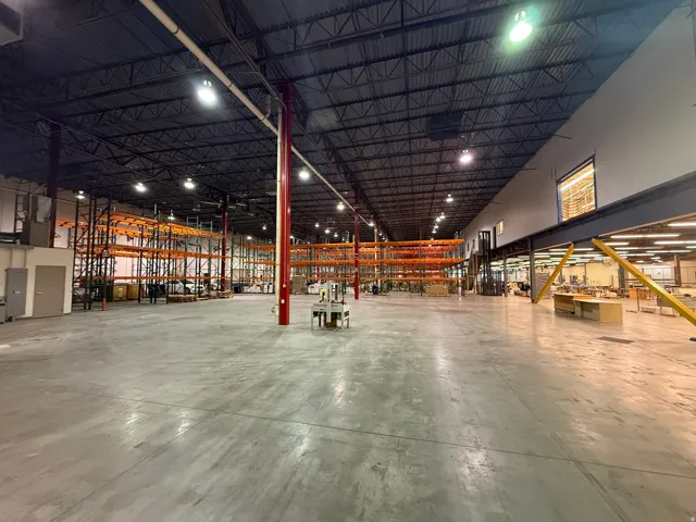 Expansive warehouse space featuring a polished concrete floor, high exposed truss ceiling, industrial lighting, and integrated mezzanine level