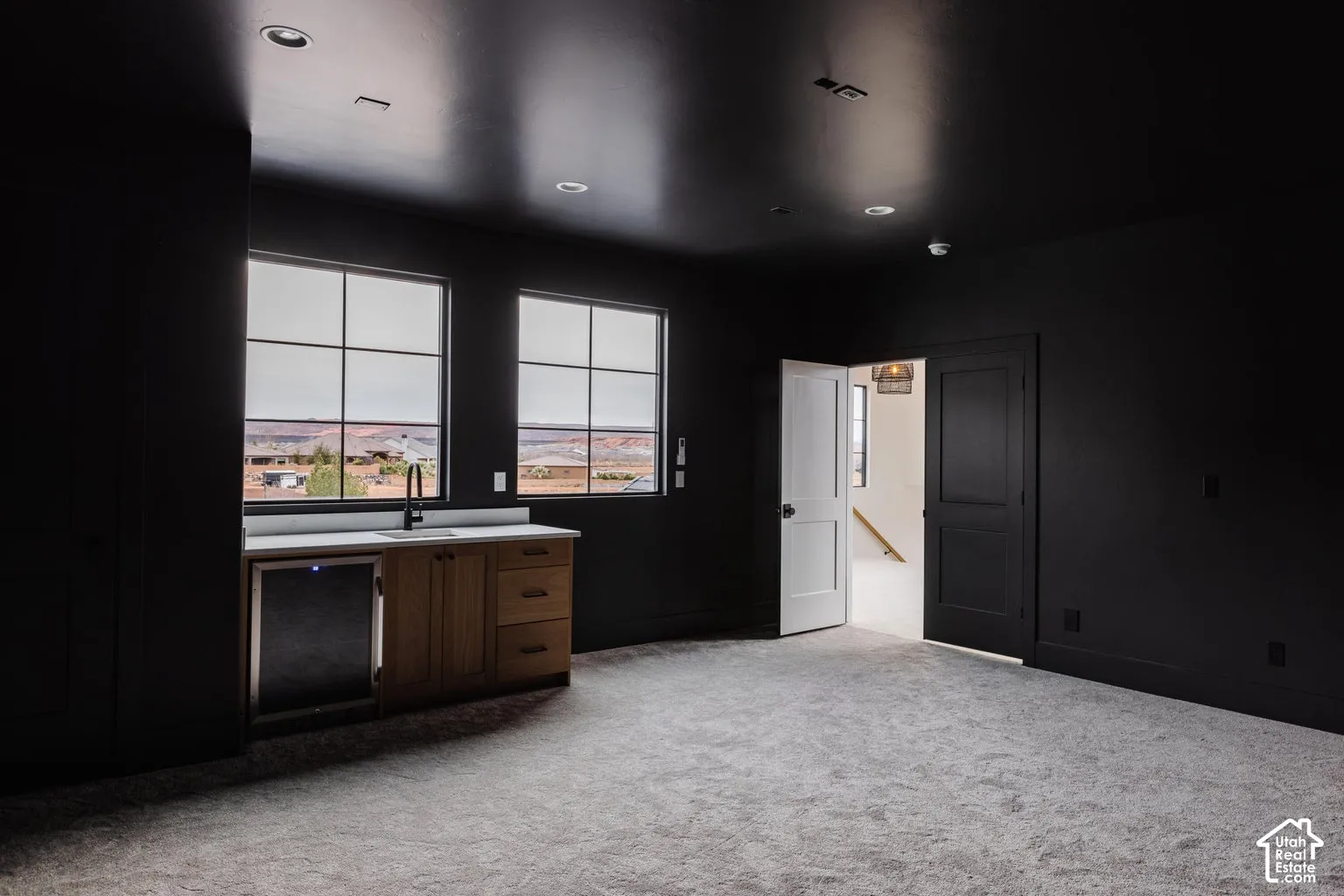 Spacious room featuring two large grid windows, a built-in wet bar with wood-finish cabinetry, a built-in beverage refrigerator, and a light-colored carpet