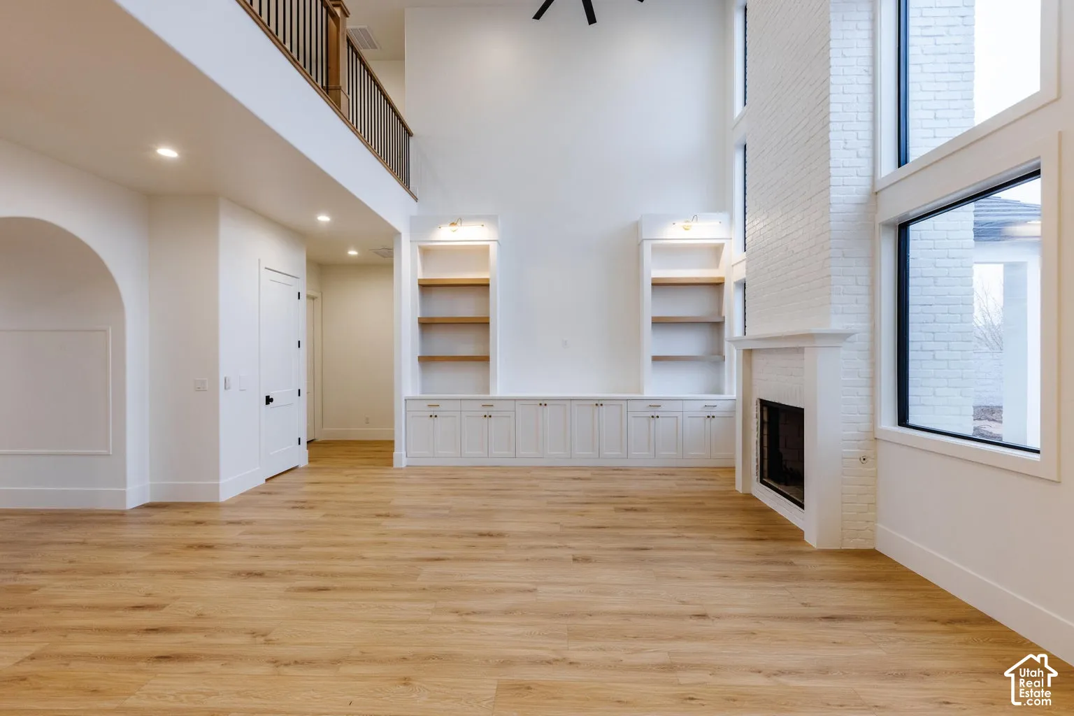 Spacious living area featuring high ceilings, light wood-finish flooring, and a floor-to-ceiling white brick fireplace