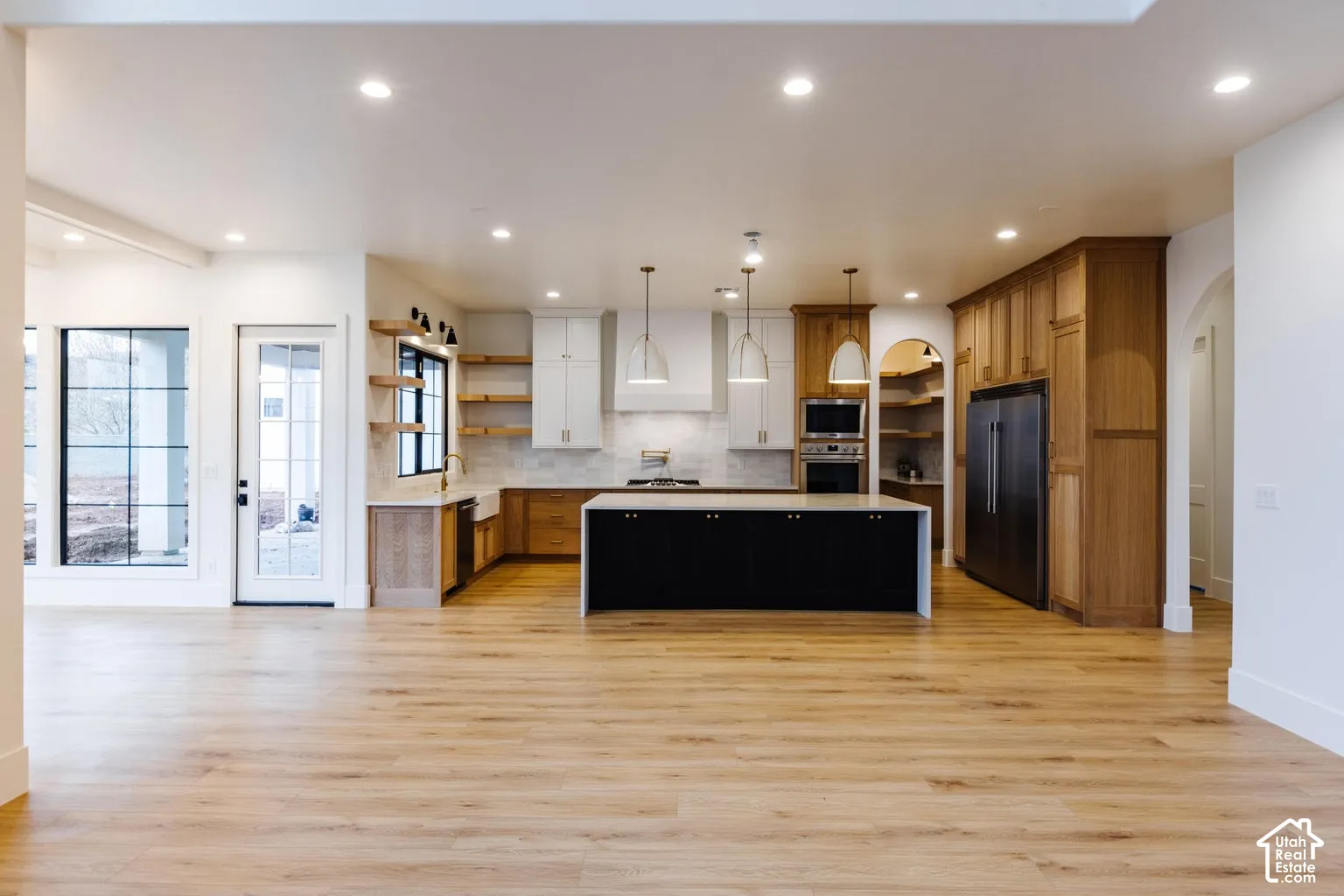 Open-concept kitchen featuring light wood-finish flooring, a central island with a black base, and a mix of light and dark wood cabinetry