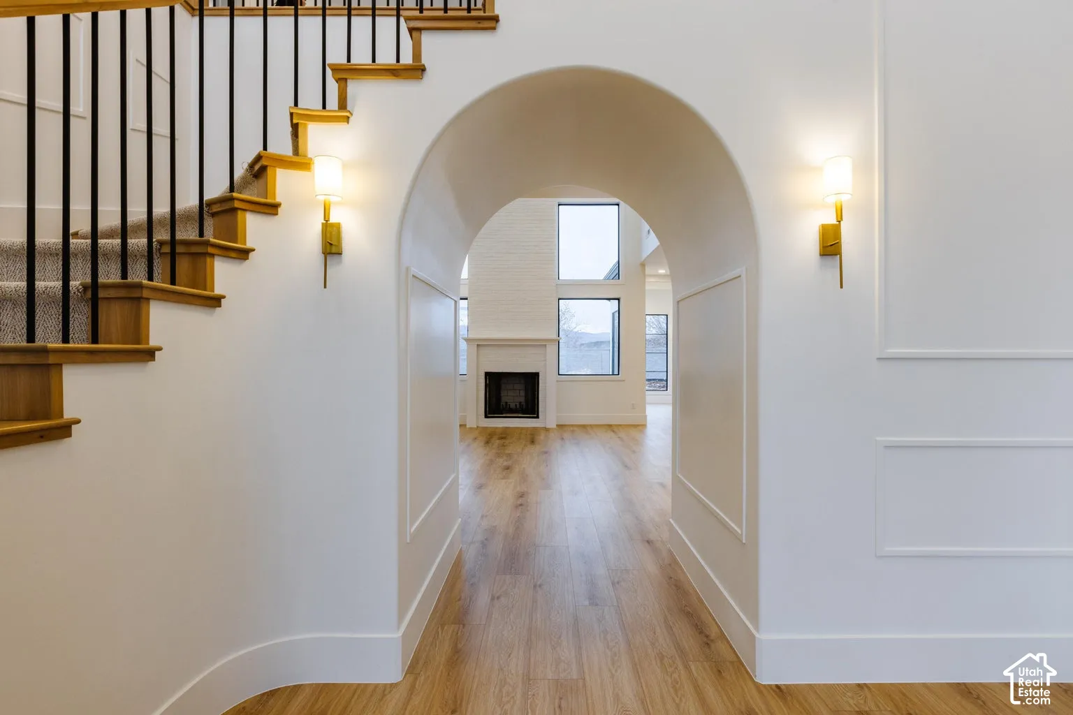 Archway entry featuring wood-finish flooring, white paneled walls, and brass wall sconces