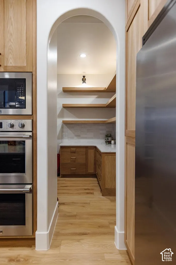 Archway entrance to a pantry featuring wood-finish flooring, recessed lighting, floating wood shelving, wood cabinetry, and stainless steel appliances