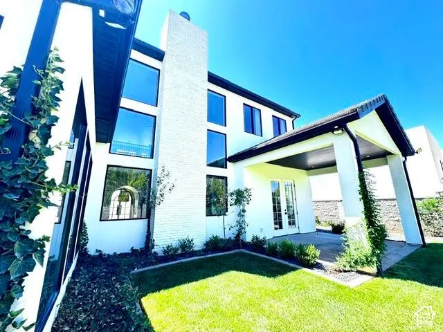 Contemporary exterior featuring white stucco, black trim windows, a prominent brick chimney, and a covered patio with French doors