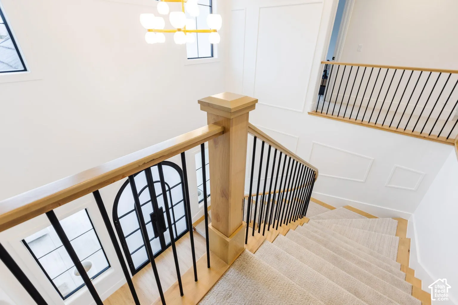 Stairwell featuring light wood handrails, black metal balusters, and a carpeted staircase