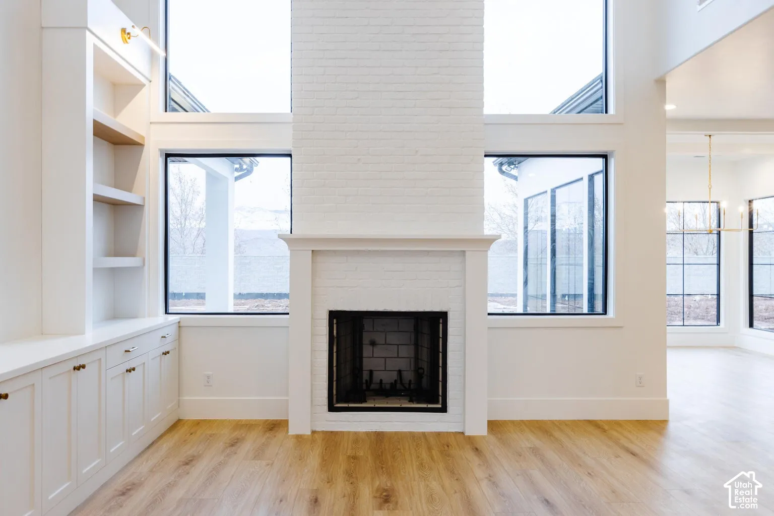 Two-story living area featuring a white brick fireplace with a mantel, built-in shelving with base cabinetry, wood-finish flooring, and expansive windows