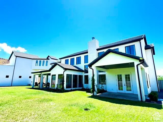 Expansive rear exterior featuring a large grassy lawn, covered patio, and multiple large windows