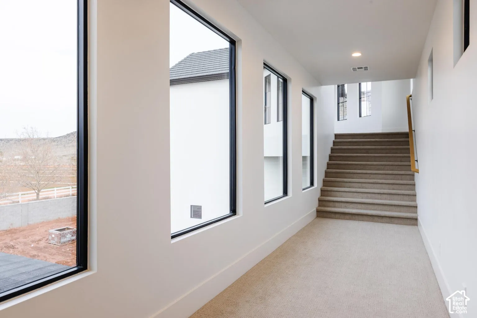 Carpeted hallway with a staircase featuring a wood handrail