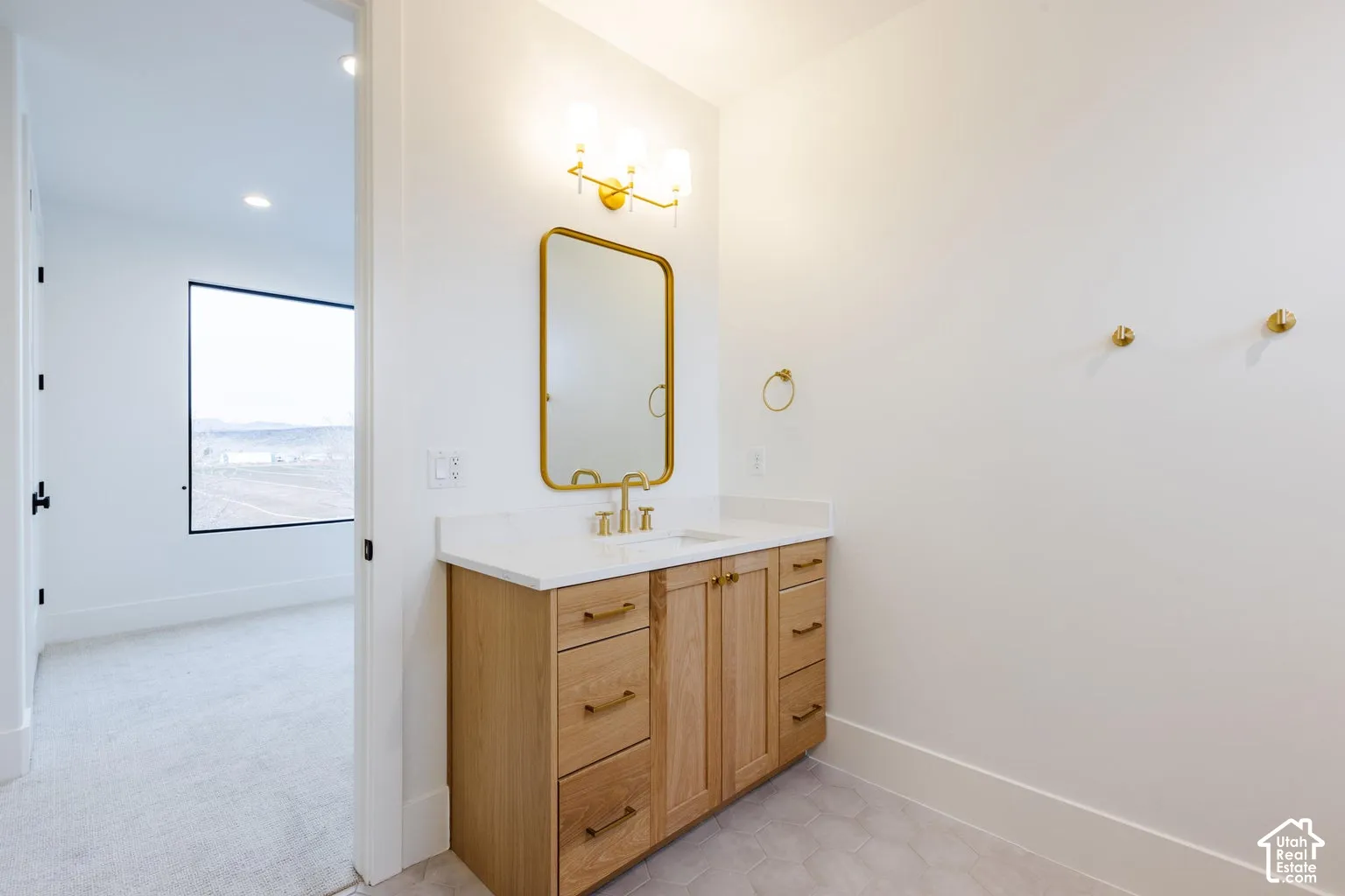 Modern bathroom vanity featuring light wood cabinetry with gold hardware, a white countertop, and a rectangular gold-framed mirror
