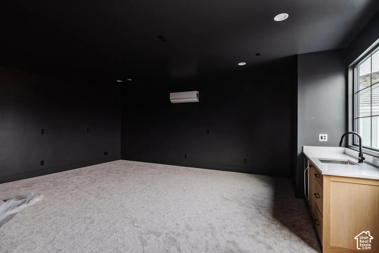Spacious interior room featuring dark-toned walls, recessed ceiling lighting, and a light-colored carpeted floor