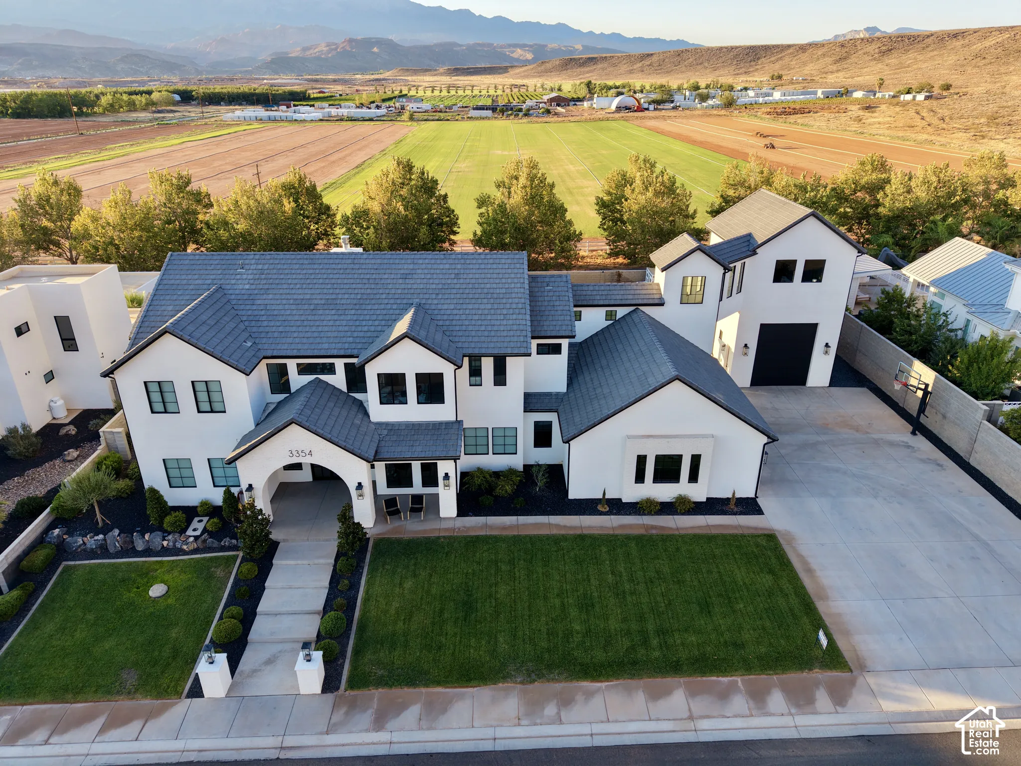 Striking contemporary residence featuring a clean-lined white exterior with dark metal roof accents, multi-level architectural design, and expansive front-facing driveway