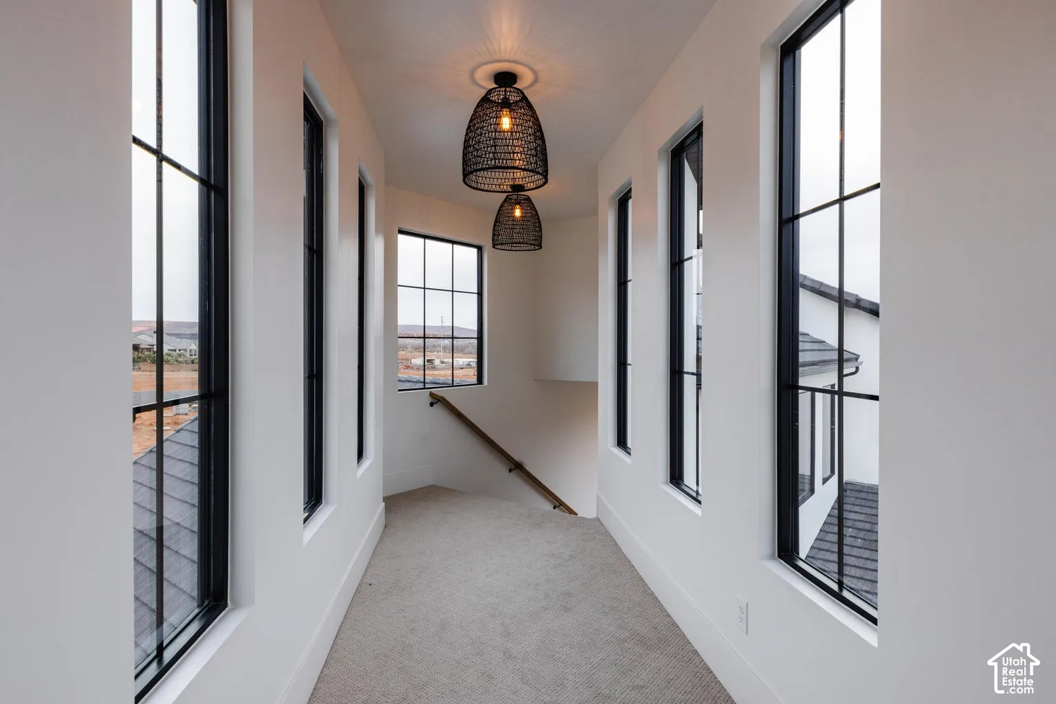 Upper-level hallway with multiple black-framed grid windows, light carpet flooring, and two woven pendant light fixtures