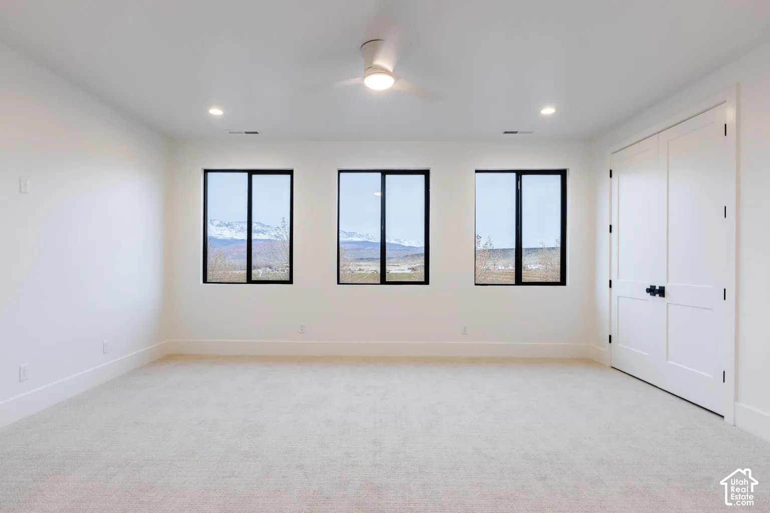 Bright room featuring three large windows with mountain scenery, neutral carpet, a contemporary ceiling fan, recessed lighting, and double bi-fold doors with black hardware