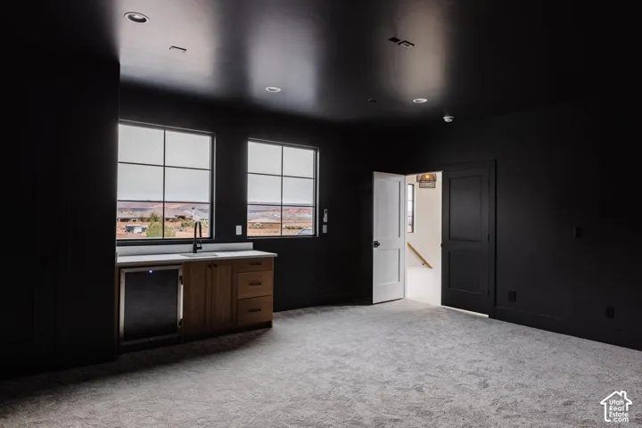 Spacious room featuring two large grid windows, a built-in wet bar with wood-finish cabinetry, a built-in beverage refrigerator, and a light-colored carpet